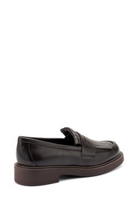 Zapatilla de charol marrón oscuro con tacón elevado, flecos decorativos en la parte superior y costuras visibles a lo largo de los bordes sobre un fondo blanco.