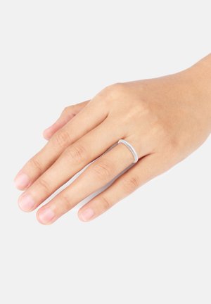 Thin silver ring on a hand, featuring a smooth surface and rounded edges, set against a plain background. Fingernails are natural and unpolished.