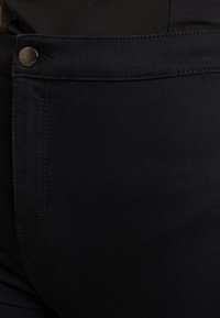 Jeans de denim negro con bolsillo delantero, cierre de botón metálico y costuras planas, que resaltan una textura suave y un tejido resistente.