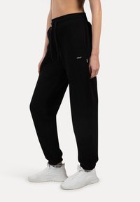 Sorte sweatpants lavet af blødt materiale med snor i taljen, sidelommer og et diskret logo på venstre lår.