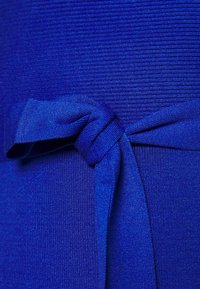 Gros plan d’un tissu texturé bleu vif avec un nœud plat soigneusement noué au centre.