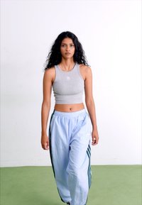 Halliga hall crop top koos logoga, kombineeritud helesiniste treeningpükstega, millel on tumerohelised külje triibud. Sile kangas ja mugav lõige.