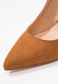 Chaussure plate en daim marron à bout pointu avec doublure intérieure lisse sur fond blanc.