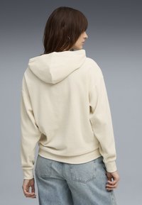 Creme ribbet hættejakke med snoretræk i hætten, afslappet pasform og lange ærmer. Parret med lyseblå høj talje denim jeans.