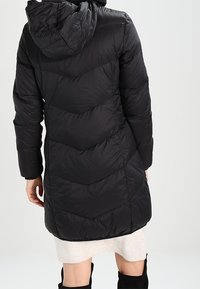 Zwarte pufferjas met een capuchon, voorzien van chevronstiksel en een gladde textuur. Halflange uitvoering met lange mouwen en zijzakken.