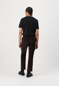 Svart kortärmad t-shirt matchad med bruna mocka tapered byxor, med sidofickor och bakfickor med knappar, bärs med svarta skor.