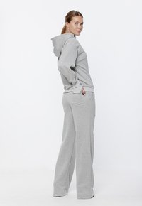 Szara bluza z kapturem i dopasowane dresy wykonane z miękkiego, szczotkowanego materiału. Bluza posiada przednią kieszeń i regulowany sznurek.