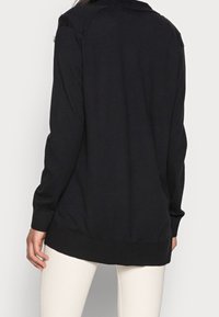 Maglia nera a maniche lunghe con orlo arrotondato e polsini a coste, realizzata in tessuto morbido, con colletto classico e vestibilità rilassata.