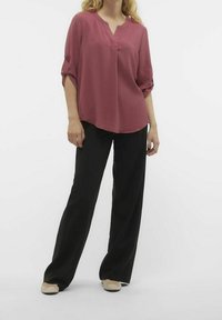 Blouse rose texturée avec un décolleté en V et des manches roulées, assortie à un pantalon large noir et des ballerines de couleur claire.