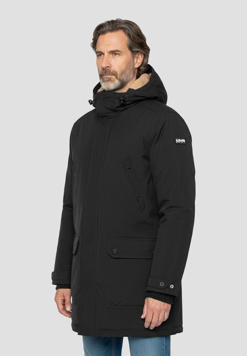 Parka noire matelassée avec capuche, tissu texturé, fermeture éclair devant et boutons-pression, ainsi que deux poches latérales. Doublée de polaire beige.