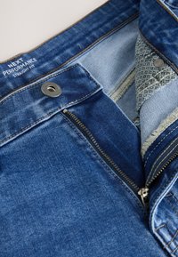 Denim-Jeans mit geöffnetem Reißverschluss und Knopfverschluss, mit dem Aufdruck „NEXT PERFORMANCE STRAIGHT FIT“ am Bund innen.