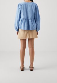 Ljusblå, randig peplumtop med puffärmar, matchad med en beige kjol. Ljusbruna sandaler med remmar bärs på bara ben.