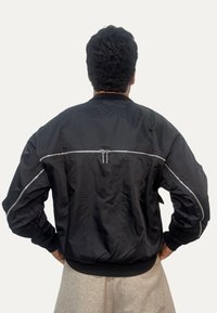 Bomber nero in tessuto liscio, con tasca con cerniera sul retro e zip argento a contrasto su polsini e maniche.