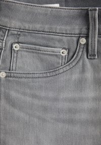 Tela de mezclilla gris con un bolsillo que presenta acentos de hardware plateado y detalles de costura en contraste, mostrando una textura suave.