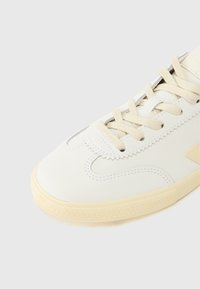 Λευκό δερμάτινο αθλητικό παπούτσι με υφή κρέμας στη σόλα από καουτσούκ, με μπεζ κορδόνια και λεπτές ραφές κατά μήκο ς των πλευρών.