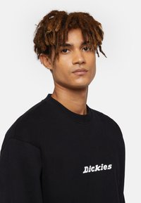 Zwart sweatshirt van zachte stof, met een ronde halslijn en een witte "Dickies"-logo gedrukt op de borst.