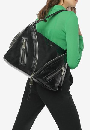 Sac en cuir noir avec une forme triangulaire unique, comportant plusieurs poches zippées et des accents en matériel argenté, porté sur un top vert.
