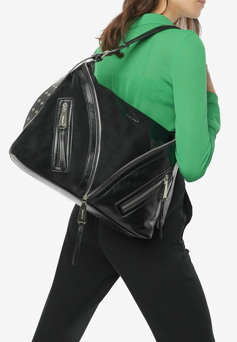 Sac en cuir noir avec une forme triangulaire unique, comportant plusieurs poches zippées et des accents en matériel argenté, porté sur un top vert.