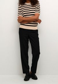 Striped striktrøje i beige og mørkebrun, korte ærmer, med en tætsiddende talje. Kombineret med sorte skrædderbukser og skinnende sorte sko.