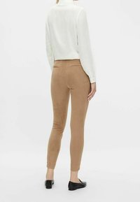 Brązowe, dopasowane legginsy wykonane z miękkiego, teksturowanego materiału, z mid-rise i tylnymi kieszeniami, zestawione z białą, długorękawową bluzką.