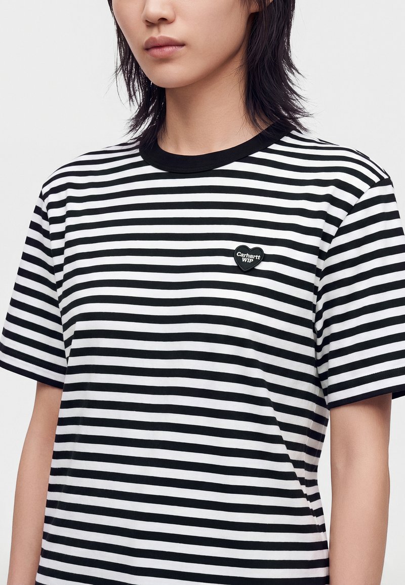 Persona che indossa una maglietta a righe orizzontali bianca e nera con un piccolo logo a forma di cuore Carhartt WIP sul petto sinistro.