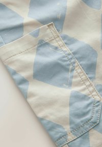 Tejido de algodón con una base beige claro que presenta formas abstractas azules. Incluye un detalle de bolsillo cosido en un lado. Acabado texturizado.