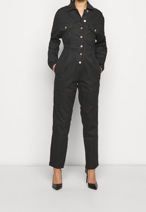 Musta haalari kestävästä kankaasta, jossa on kaulus, etunapit, kaksi rintataskua ja vartaloa myötäilevä vyötärömalli.