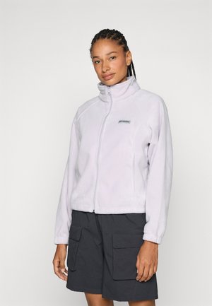 Vaaleanliila fleece-takki korkealla kauluksella, edessä vetoketju ja logo vasemmassa rinnassa. Yhdistetty tummiin cargo-shortseihin.
