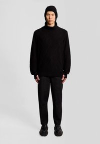 Fekete, steppelt, túlméretes pulóver magas nyakkal, fekete mintás nadrággal és fekete fűzős cipővel párosítva. Egyszerű kialakítás, minimális kiegészítők.