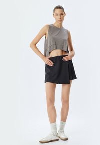 Top corto grigio, gonna mini nera con cintura elastica e sneakers bianche con dettagli beige; texture morbide e design semplice.