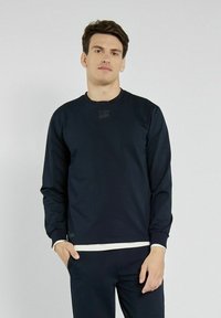 Granatowy sweatshirt z okrągłym dekoltem i długimi rękawami. Posiada subtelny nadruk logo na piersi oraz teksturowane wykończenie materiału.
