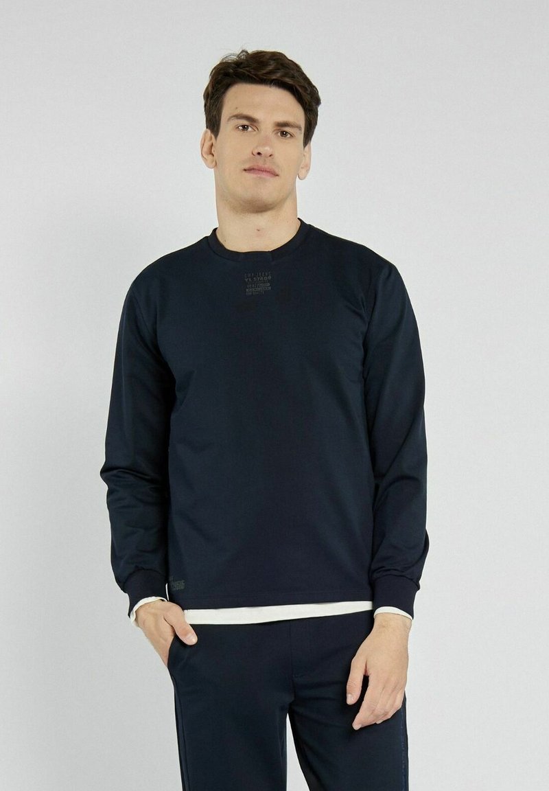Granatowy sweatshirt z okrągłym dekoltem i długimi rękawami. Posiada subtelny nadruk logo na piersi oraz teksturowane wykończenie materiału.