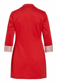 Palton roșu cu mâneci lungi, cu manșete întoarse care arată un material alb cu dungi roșii, cusătură dreaptă pe spate și guler.