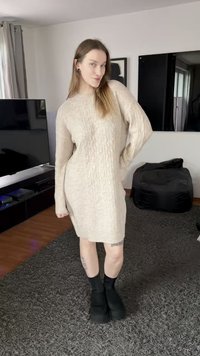 Knitted beige sweater dress with a cable pattern, long sleeves, and a loose fit, paired with black platform shoes and crew socks.