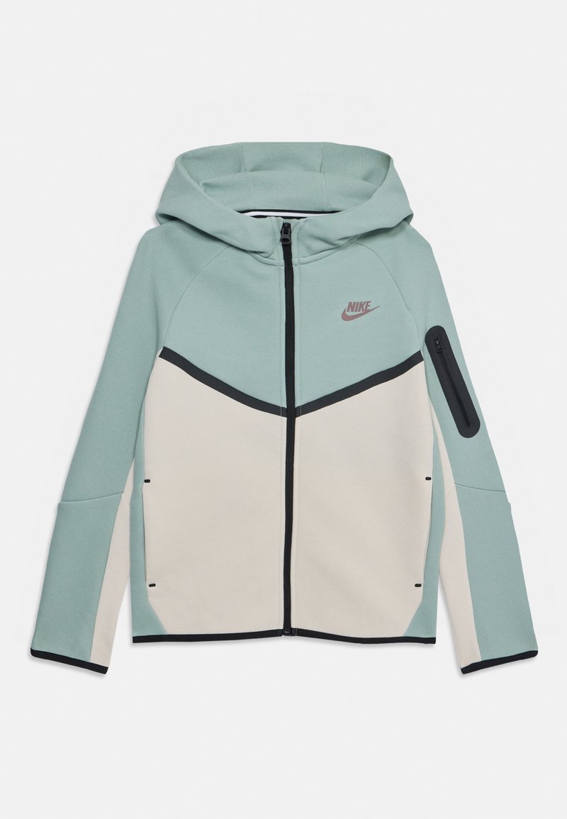 Capucha σε ανοιχτό γαλάζιο και κρέμα. Διαθέτει μπροστινό φερμουάρ, αντίθετους μαύρους τόνους και τσέπη στον ώμο με φερμουάρ για αποθήκευση.