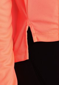 Korallfarbener Sport-Top mit seitlichem Schlitz, aus dehnbarem Stoff, mit kontrastierendem schwarzem Unterteil. Glatte Textur und figurbetontes Design.