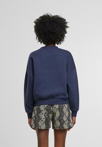 Námořnická modrá mikina s kulatým výstřihem, spadlými rameny a žebrovanými manžetami, spárovaná s šortkami s hadím potiskem.