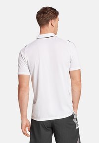 Maglietta polo bianca a maniche corte, con accenti neri a contrasto sul colletto e sulle spalle, realizzata in tessuto liscio. Visibile la vista posteriore.