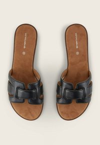 Sandales à glisser en cuir noir avec une large lanière présentant des découpes. Semelle intérieure douce marron avec le nom de la marque "TOM TAILOR" visible.