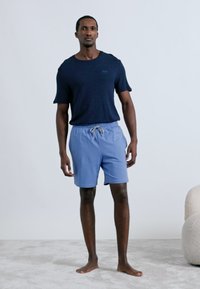 Camisa de manga curta azul-marinho combinada com calções azul claro com cordão, apresentando um ajuste folgado e textura suave do tecido. Design liso, sem padrões.