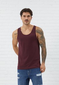Viininpunainen tanktop, jossa on pyöreä kaula-aukko, valmistettu sileästä kankaasta. Ominaisuuksiin kuuluu slim fit -malli, ja se on yhdistetty kulutettuihin sinisiin farkkuihin.