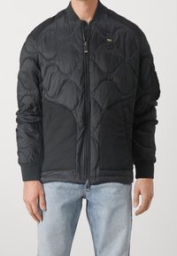 Chaqueta bomber negra con patrón acolchado, cierre de cremallera, puños de canalé y bolsillos laterales. Confeccionada en una tela suave y ligera.