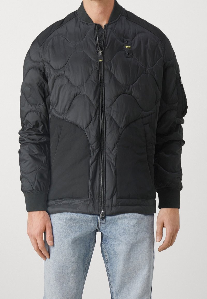 Chaqueta bomber negra con patrón acolchado, cierre de cremallera, puños de canalé y bolsillos laterales. Confeccionada en una tela suave y ligera.