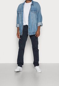 Džínová bunda světle modré barvy s knoflíkovými zapínáními a dvěma náprsními kapsami, doplněná tmavě modrými cargo kalhotami a bílými teniskami.