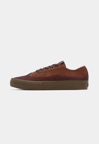 Brązowe zamszowe sneakersy z ciemniejszymi brązowymi akcentami, płaską gumową podeszwą i okrągłymi sznurówkami. Posiadają subtelną logo blisko oczek. Niski krój.