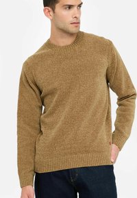 Maglione marrone lavorato a maglia con scollo a girocollo a coste e polsini, caratterizzato da un motivo testurizzato, abbinato a jeans in denim scuro.