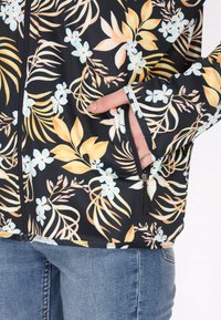 Zwarte bloemen zip-up jack, met lichtblauwe en gele bloemmotieven, een voorkantzak en contrasterende stikseldetails.