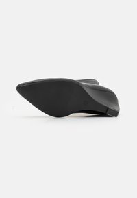 Chaussure à talon haut noire à bout pointu, avec une surface supérieure lisse et une semelle texturée, présentant un talon bloc bas pour plus de stabilité.