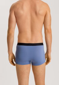 Herrars blå boxerkalsonger med svart midjeband; slät textur, åtsittande design och längd till mitten av låret. Bakifrån visar de platta sömmar.