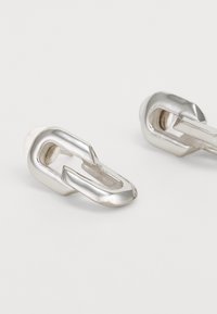 Orecchini in metallo argento con un design a catena. Superficie liscia con una finitura lucida, dotati di una sezione aperta per un tocco di dettaglio in più.